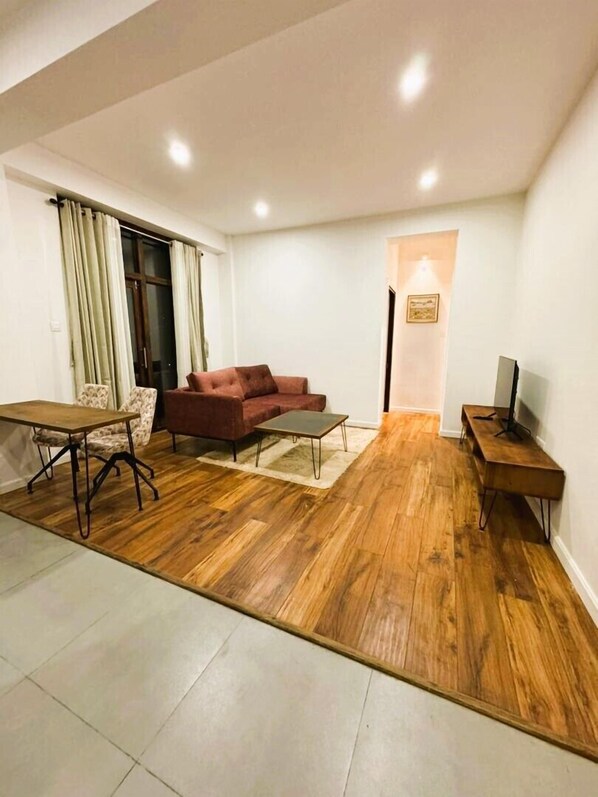 A living room with a wooden floor, a red sofa, a coffee table, a TV stand, and a dining table.