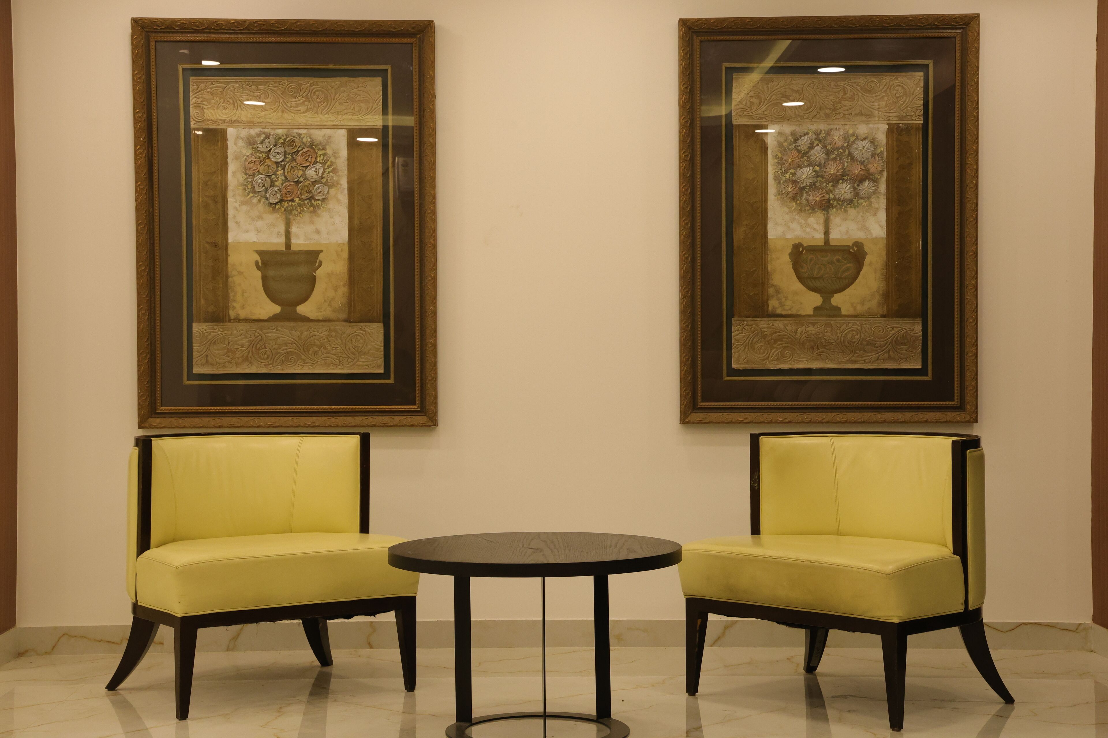 Two yellow chairs and a small round table in a room with two framed artworks on the wall.