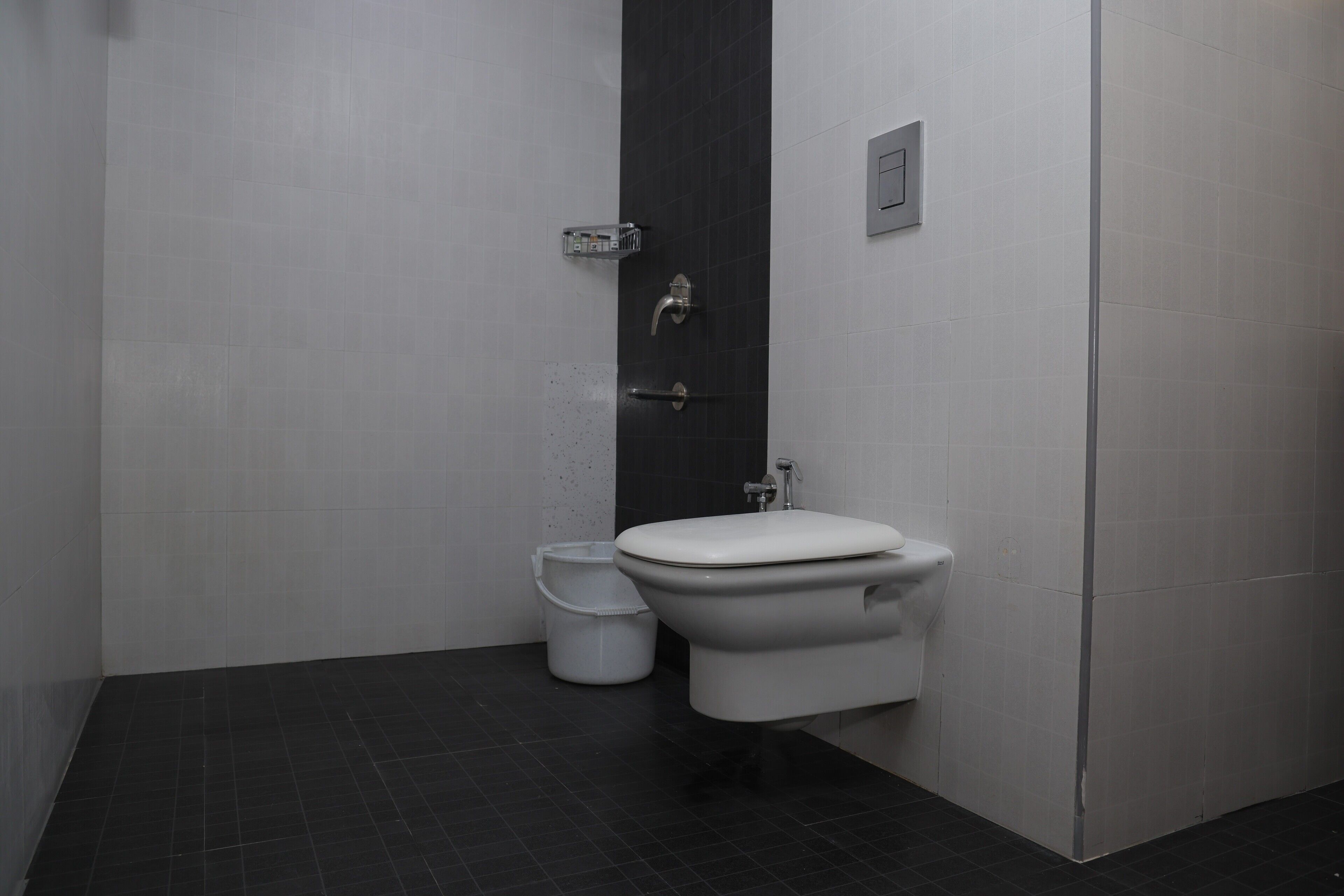 A modern bathroom with a toilet, a small trash bin, and a wall-mounted soap dispenser.
