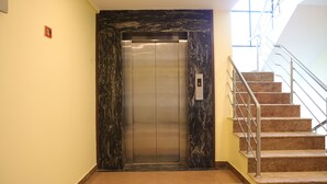 An elevator with a marble wall, a stairwell with metal railings, and a light switch on the wall. - Hotel SR Palani (Palani)