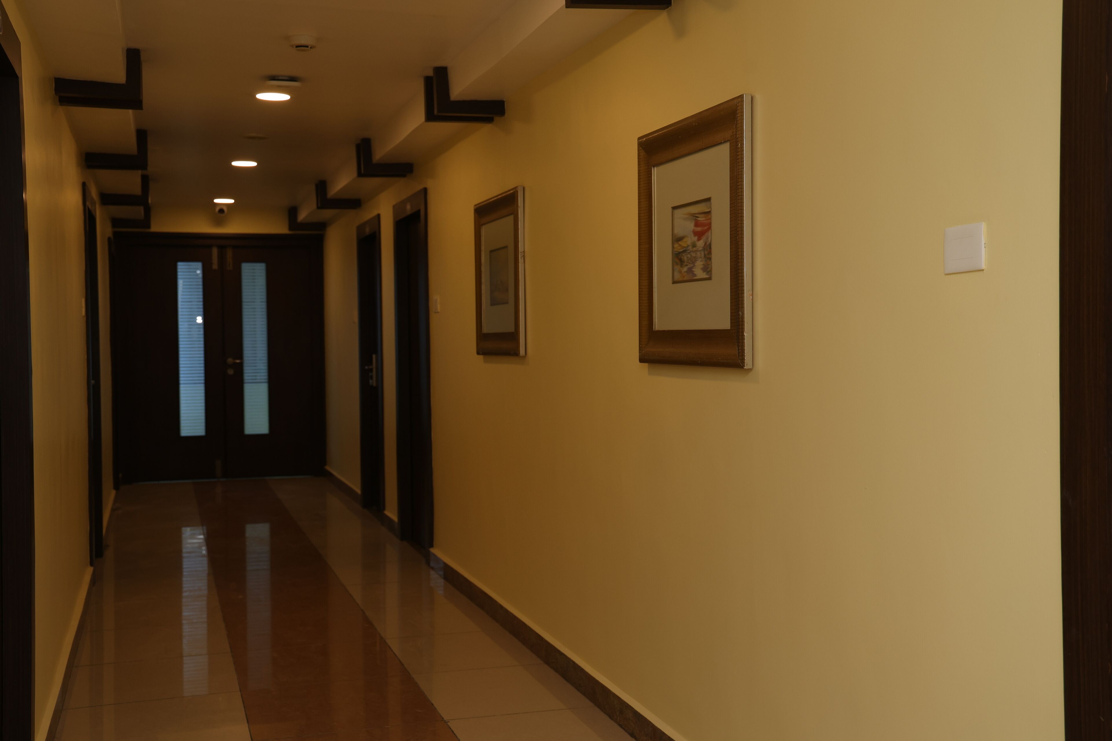 A hallway with framed artwork on the walls, a tiled floor, and doors at the end.
