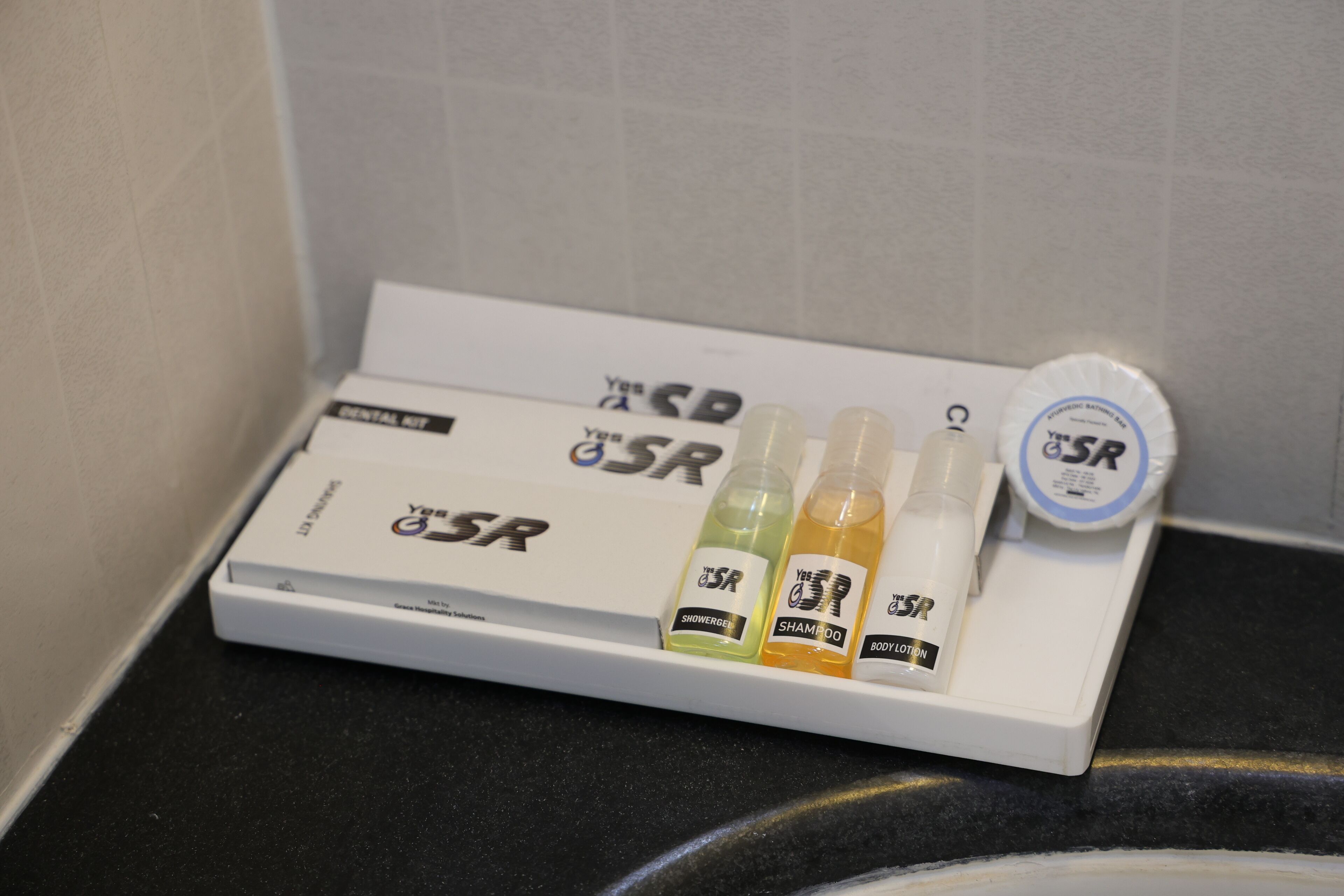 A bathroom shelf with a dental kit, shower gel, shampoo, and body lotion.