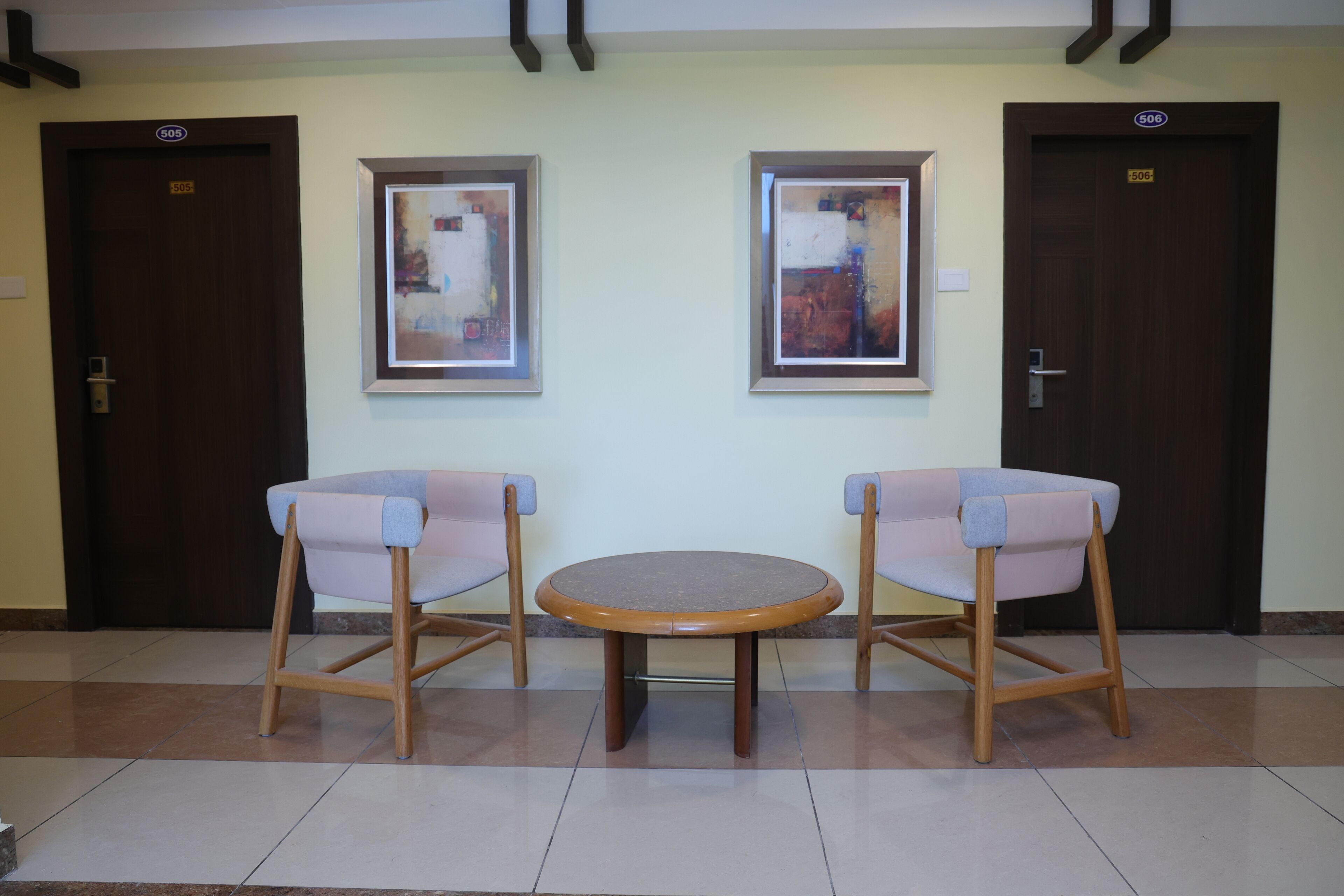 A reception area with two chairs and a table, two framed abstract paintings on the wall, and two doors with the number 505.