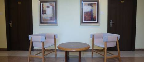 Une salle d’attente avec deux chaises et une table, deux tableaux abstraits encadrés accrochés au mur, et deux portes portant le numéro 505.