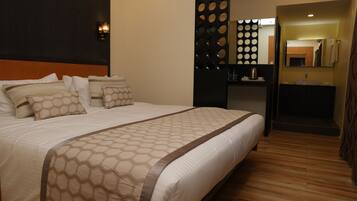A hotel room with a large bed, a wooden floor, a bathroom with a sink and mirror, and a decorative wall panel.