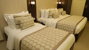 A hotel room with two beds, each with a patterned bedspread and multiple pillows. There are wall-mounted lights above the beds and a door on the right. - Hotel SR Palani (Palani)