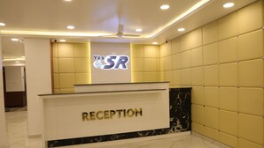 A reception area with a marble counter, a ceiling fan, and a sign that reads "Yes SR". - Hotel SR Palani (Palani)