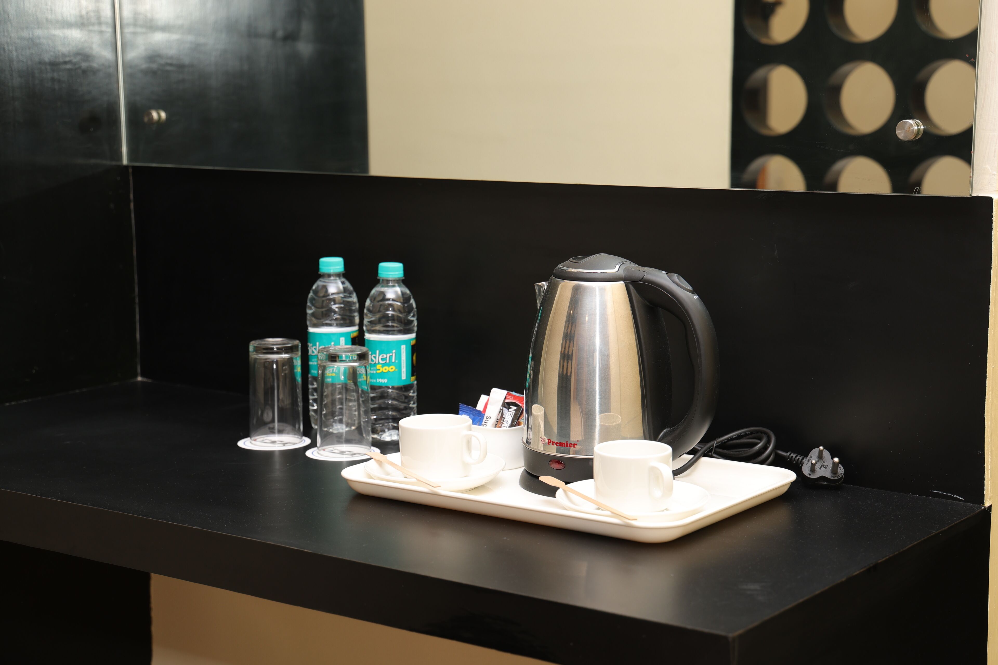 A hotel room's breakfast setup with a kettle, cups, and water bottles on a tray.
