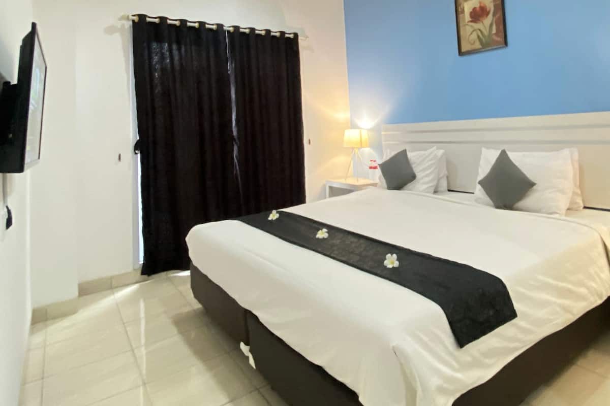 A hotel room with a large bed, a nightstand, a lamp, a painting on the wall, and a window with curtains.