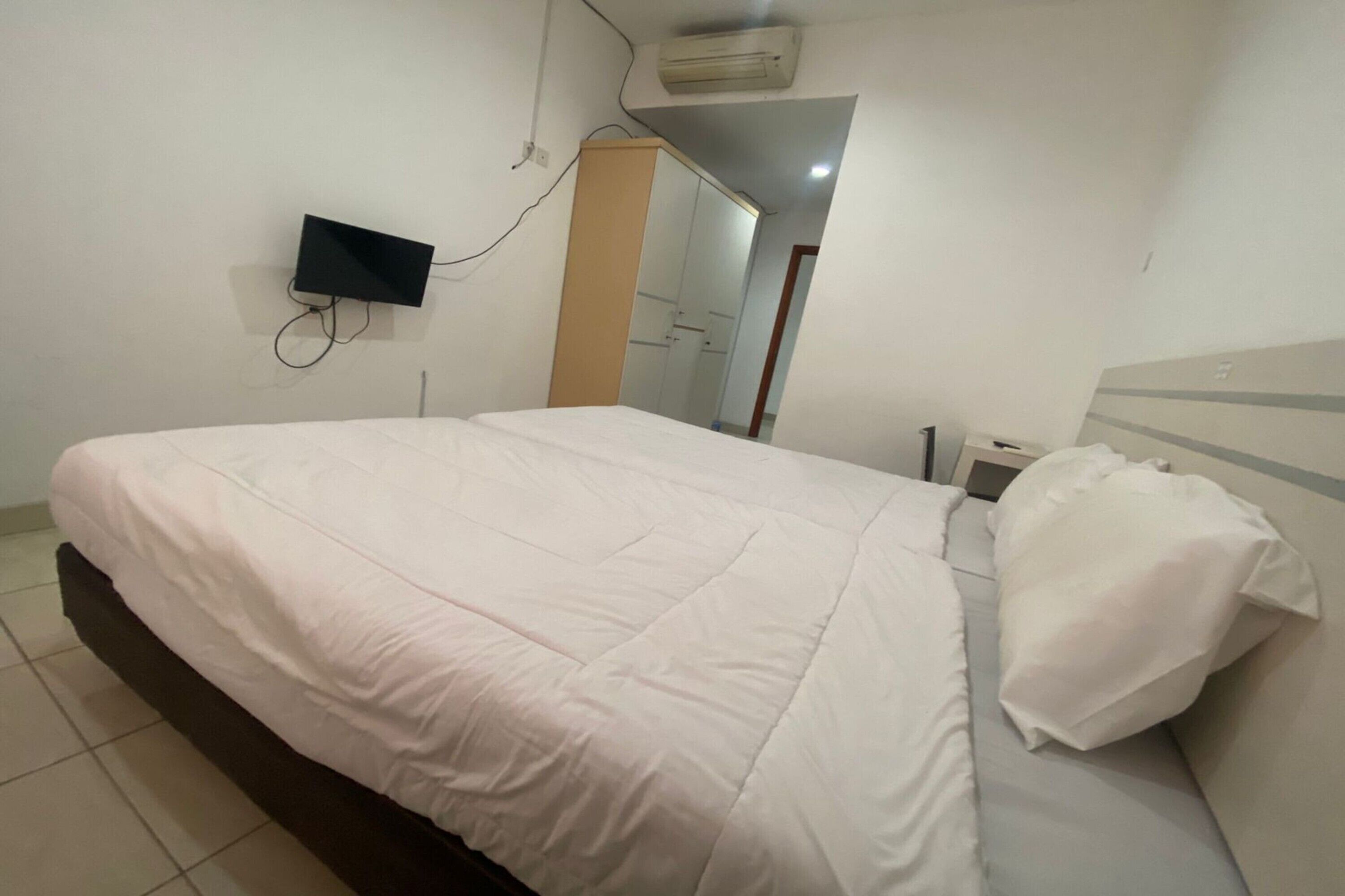 Une chambre à coucher avec un lit, un téléviseur fixé au mur, une armoire et un miroir.