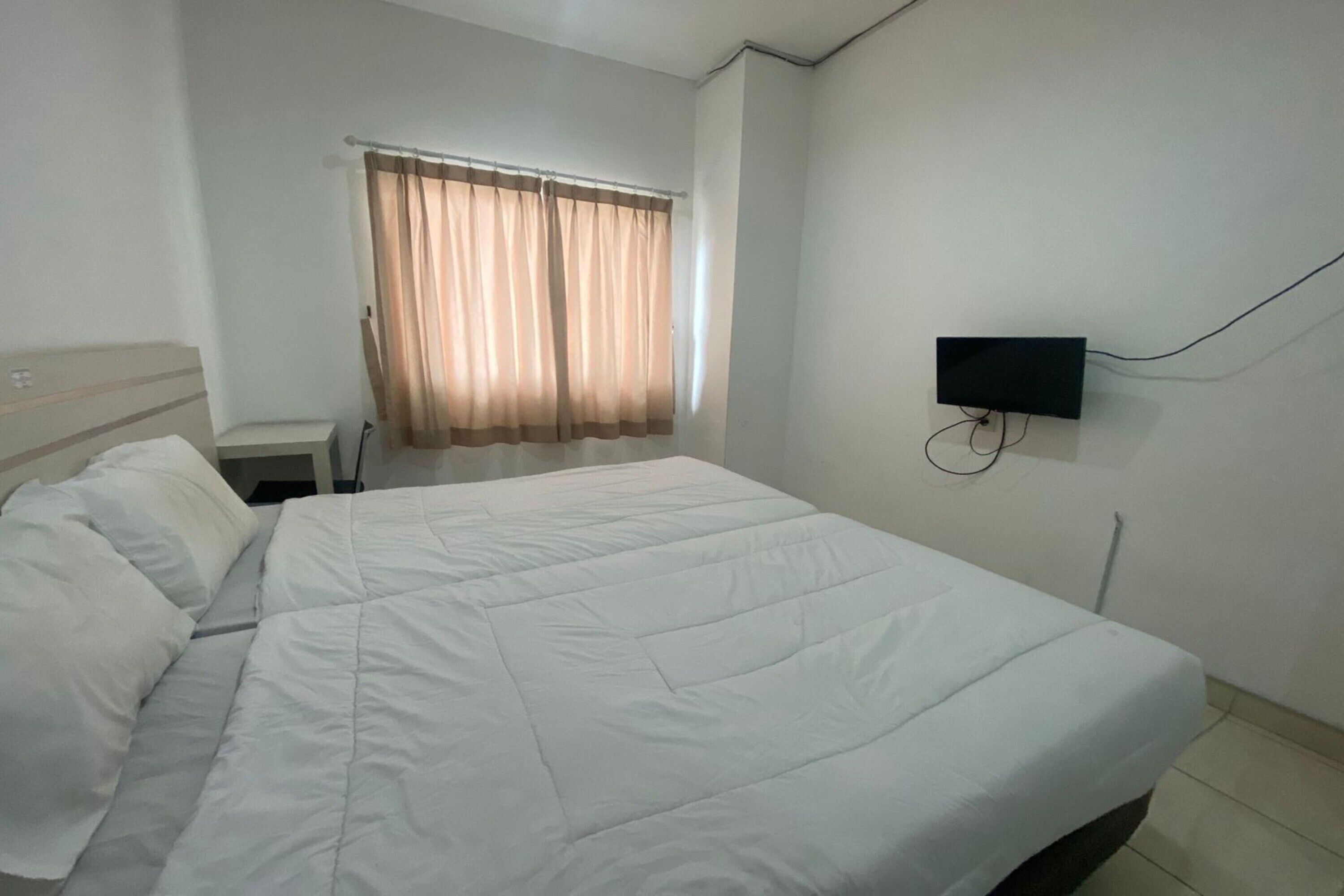 Ein Hotelzimmer mit einem großen Bett, einem an der Wand befestigten Fernseher und einem Fenster mit Vorhängen.
