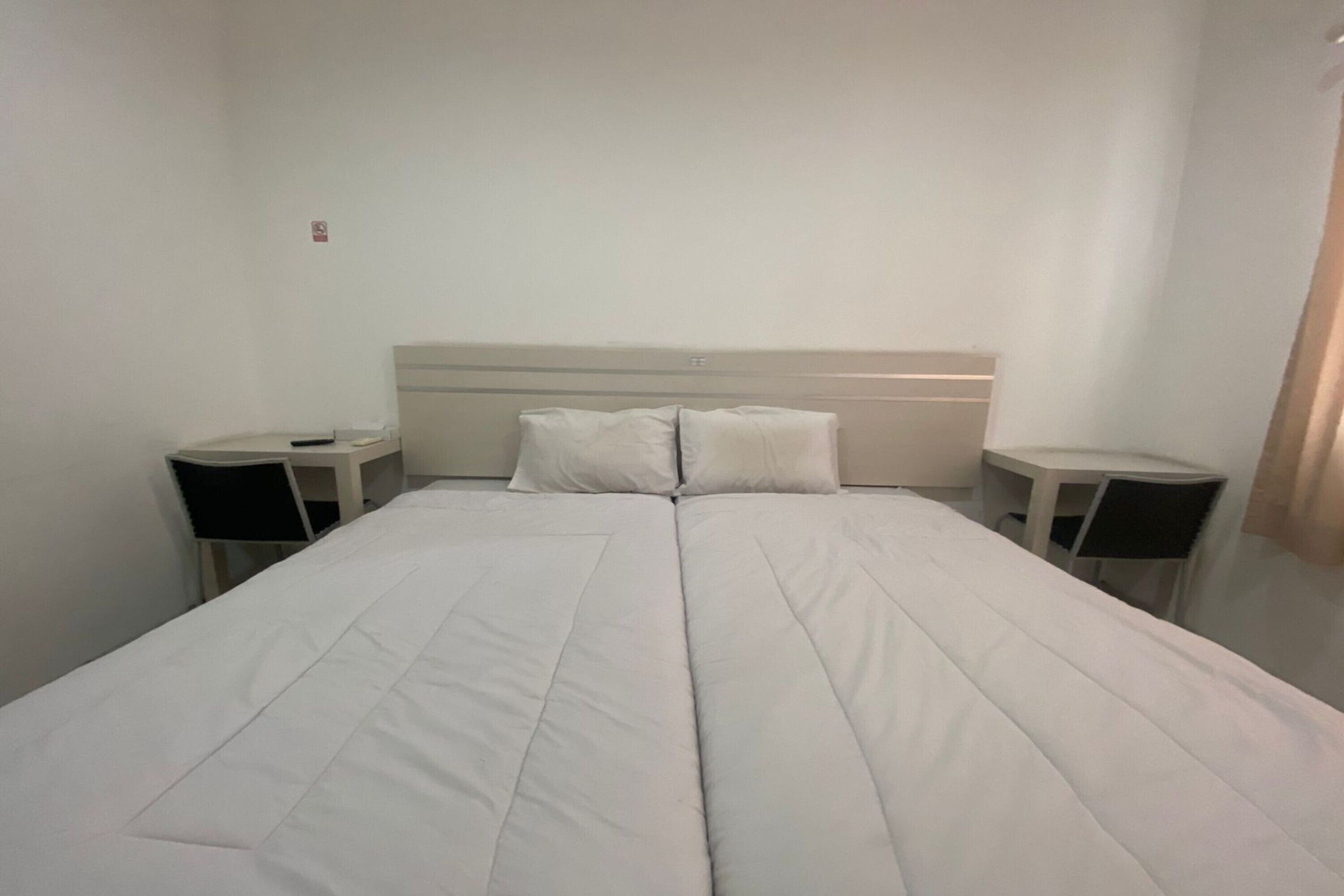 Una habitación de hotel con una cama grande, dos mesitas de noche y un cabecero.