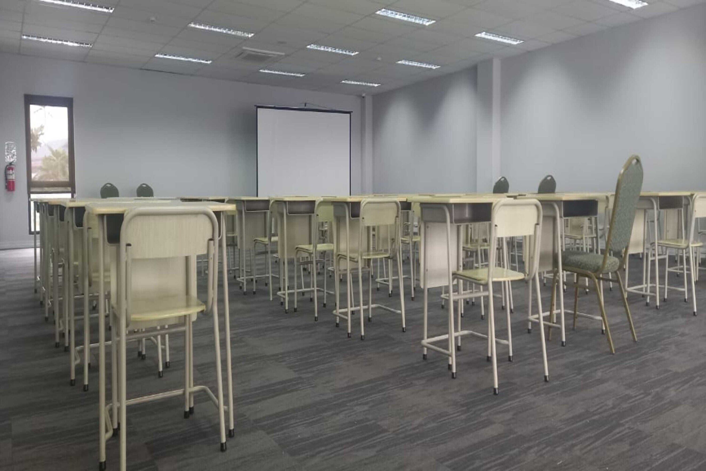 A conference room with rows of chairs and a projector screen on the wall.