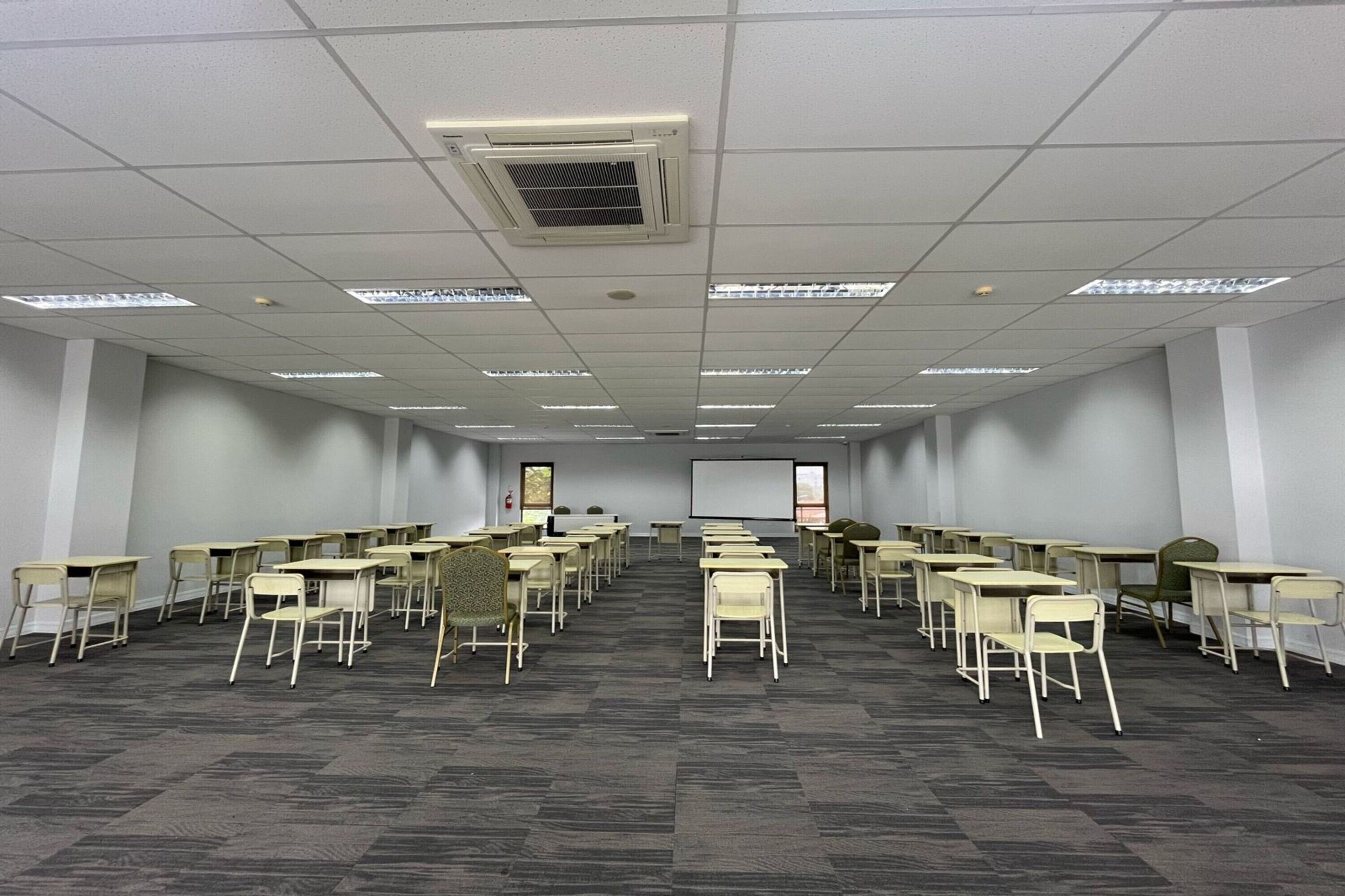 A conference room with rows of tables and chairs, a projector screen, and a whiteboard.