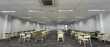 A conference room with rows of tables and chairs, a projector screen, and a whiteboard.