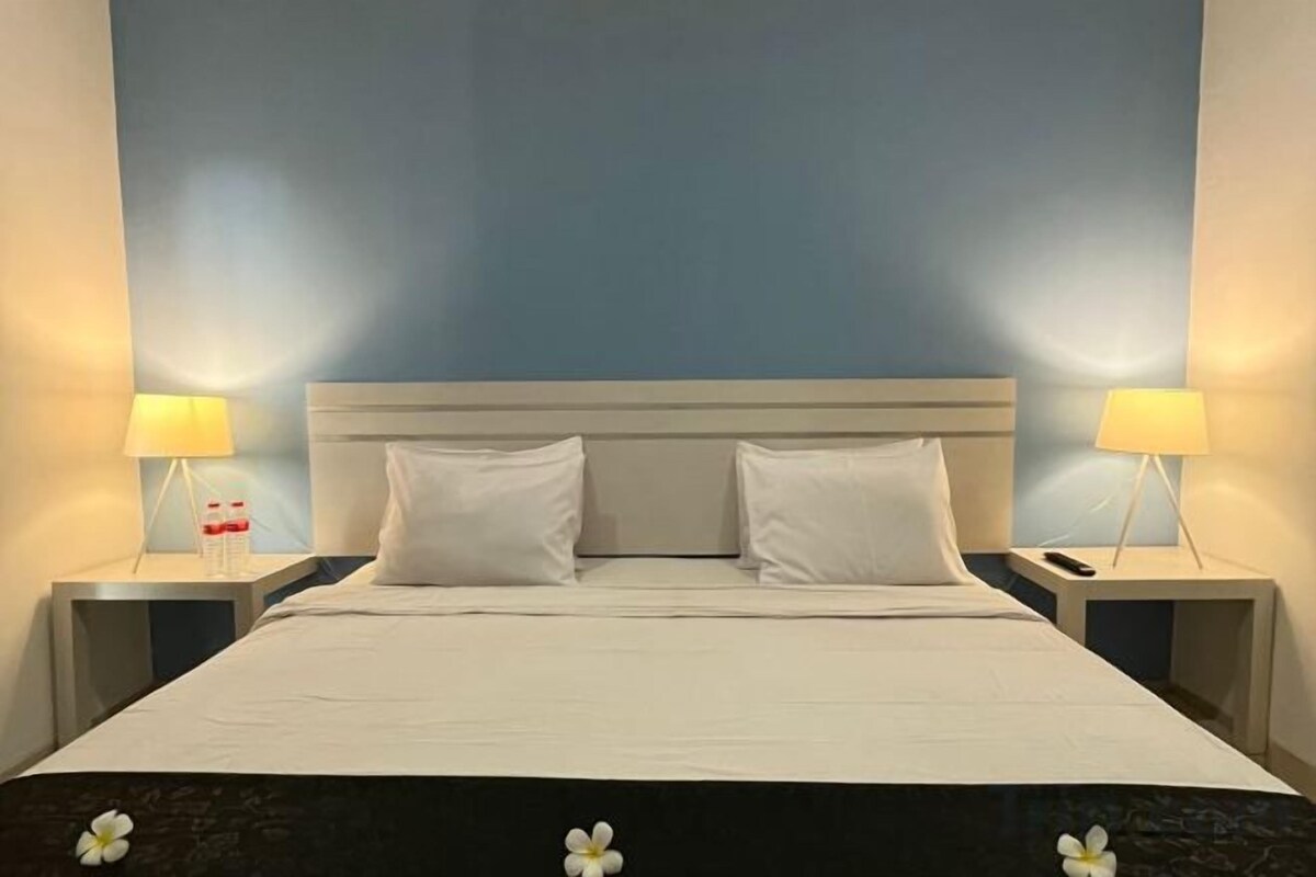 Une chambre d’hôtel avec un grand lit, deux tables de chevet avec des lampes et un mur bleu uni.