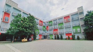 Un immeuble à plusieurs étages doté de balcons, une cour pavée et un arbre au premier plan.