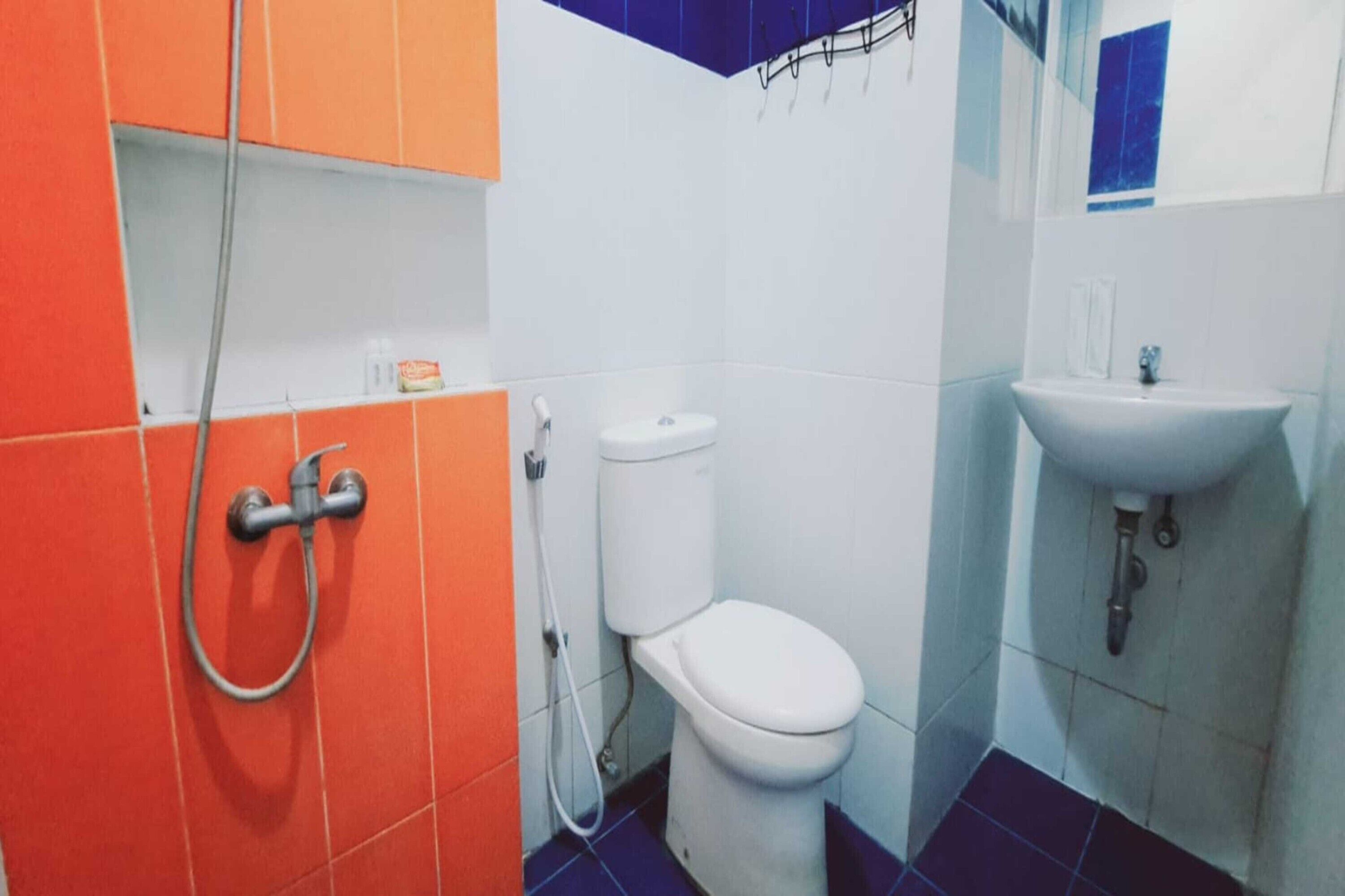 Un baño con inodoro blanco, lavamanos y ducha con manguera.