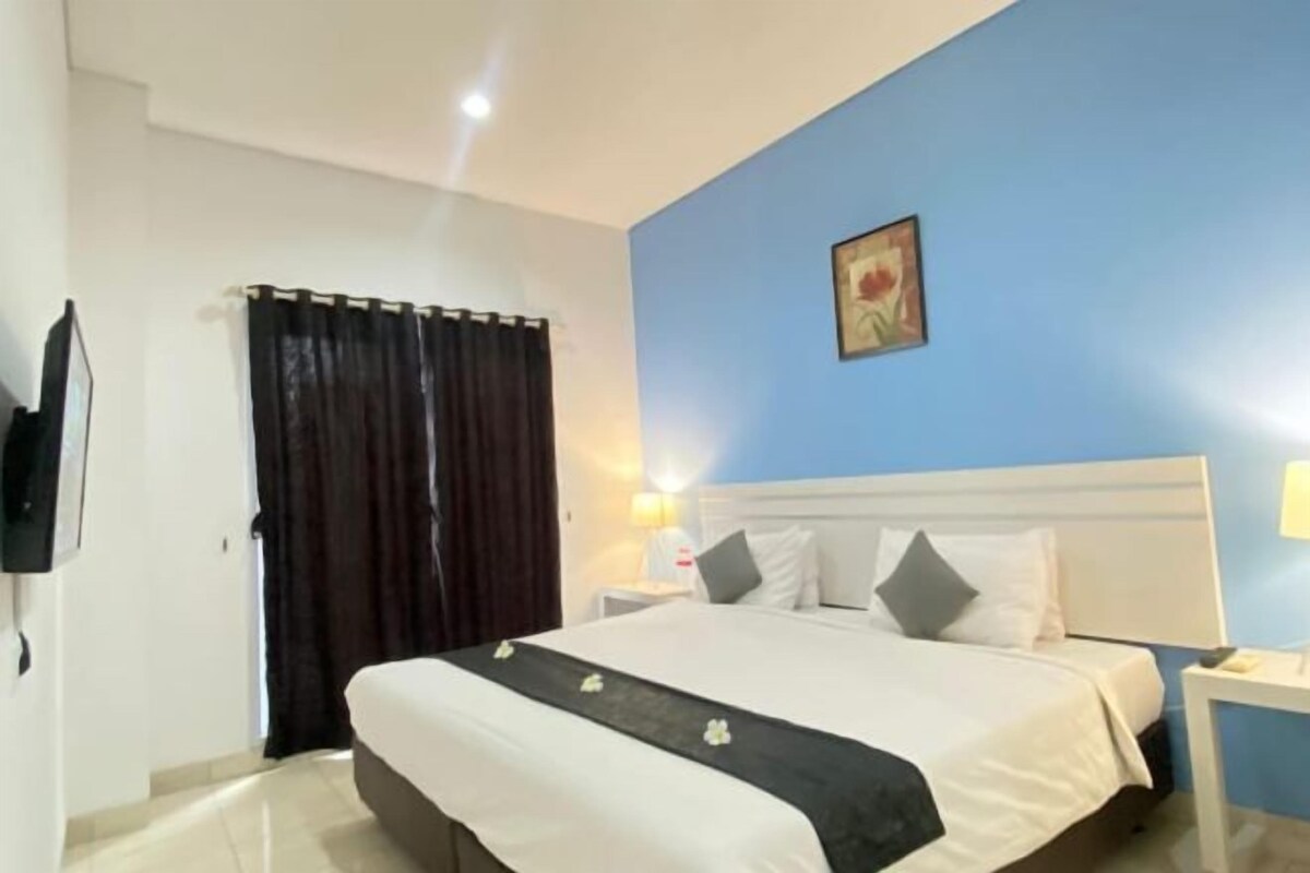 Une chambre d’hôtel avec un lit, des rideaux, un tableau au mur et une table de chevet avec une lampe.