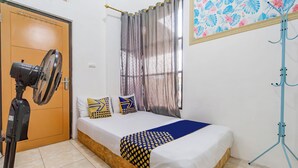 A bedroom with a bed, a standing fan, a door, and a window with curtains. - Hotel O Ita Homestay Syariah (Sidoarjo)