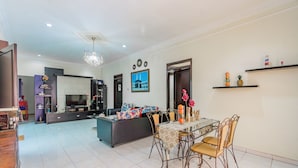 A spacious living area with a dining table, chairs, and a sofa. There is a kitchen area in the background, a chandelier, and a framed picture on the wall. - Hotel O Ita Homestay Syariah (Sidoarjo)