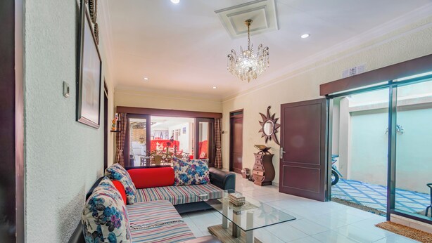 A living room with a sofa, a glass coffee table, and a chandelier. There is a door leading to another room and a view of the outside. - Hotel O Ita Homestay Syariah (Sidoarjo)