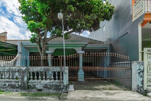 Un edificio con entrada protegida por una reja, un árbol en primer plano y un letrero con texto.