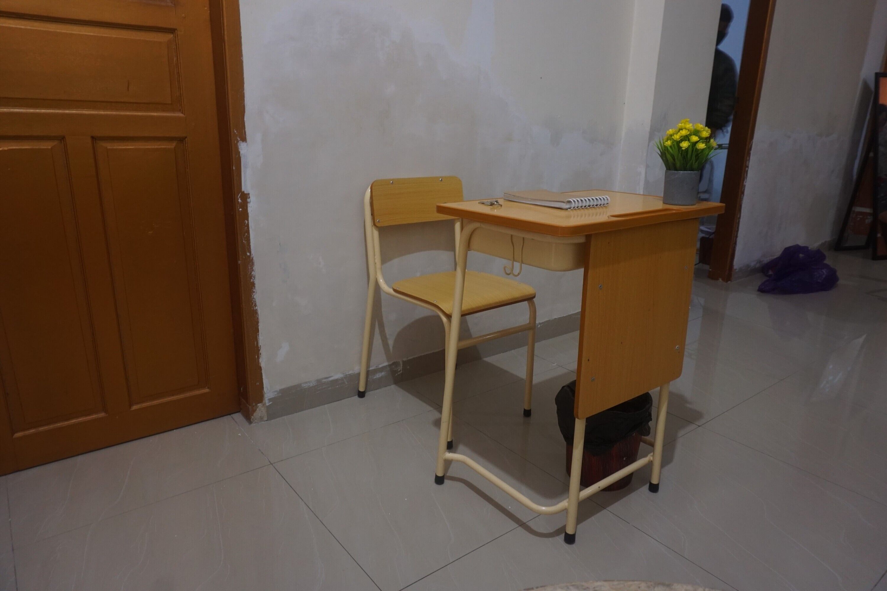 A small room with a wooden desk and chair, a mirror, and a vase with flowers.