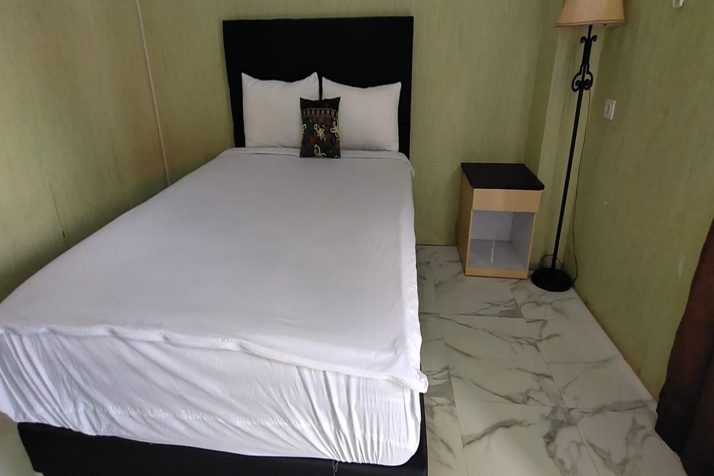 Una cama bien hecha con ropa de cama blanca, cabecera negra y un cojín decorativo.