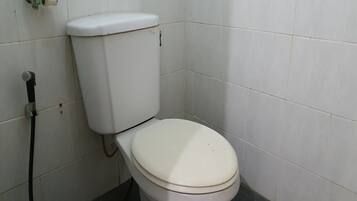 Des toilettes blanches avec un abattant fermé, une poignée de chasse d’eau visible et un tuyau d’eau visible sur le côté gauche.