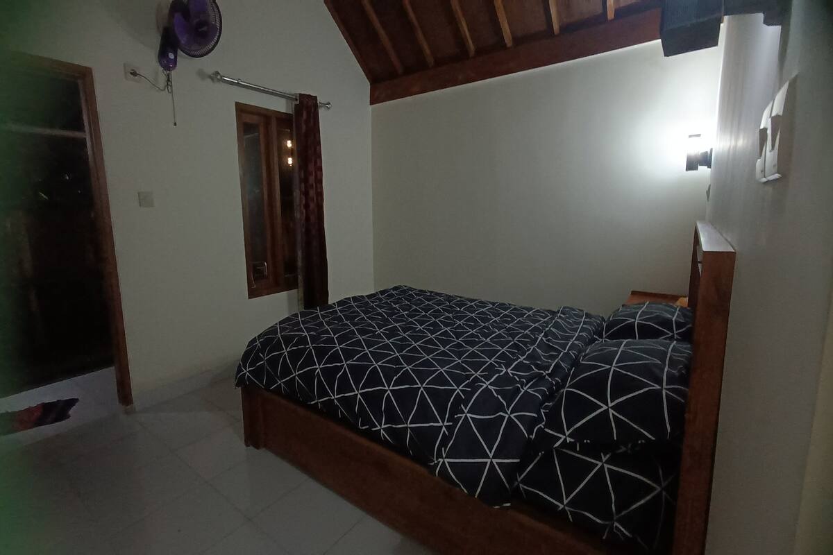 A bedroom with a bed, a window with curtains, a ceiling fan, and a light fixture.