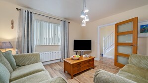 A living room with a sofa, a wooden coffee table with a bowl of fruit, a flat-screen TV, and a staircase leading to another room. - Y Deri - Close to Village and Beach (Saundersfoot)