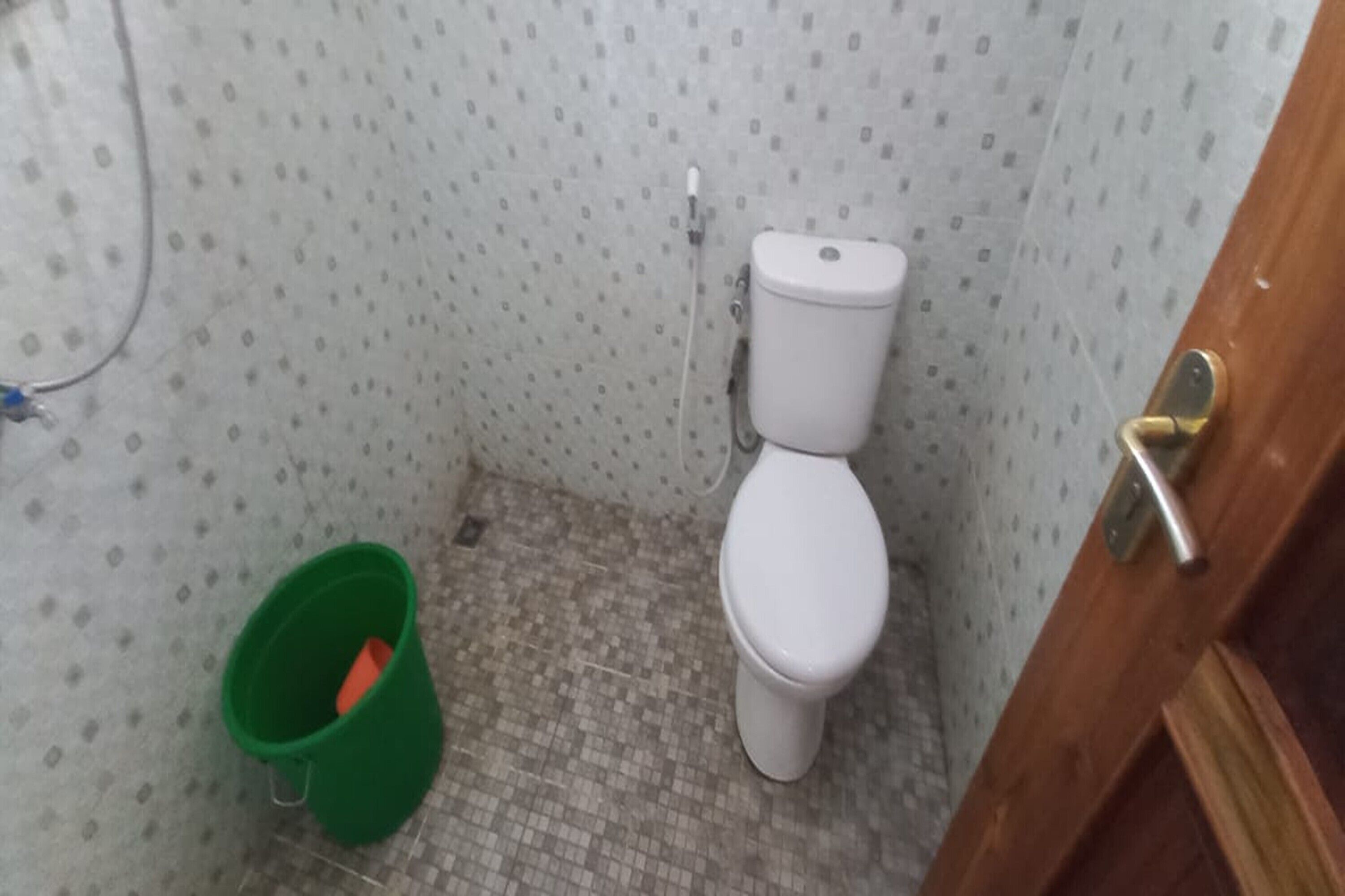 Un baño pequeño con inodoro, un cubo verde y piso de baldosas.
