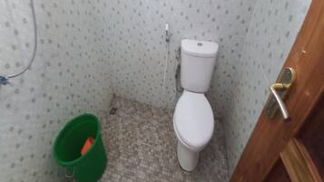 Un baño pequeño con inodoro, un cubo verde y piso de baldosas.