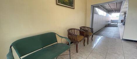 A hallway with a green bench and wooden chairs, a painting on the wall, and a view into another room.