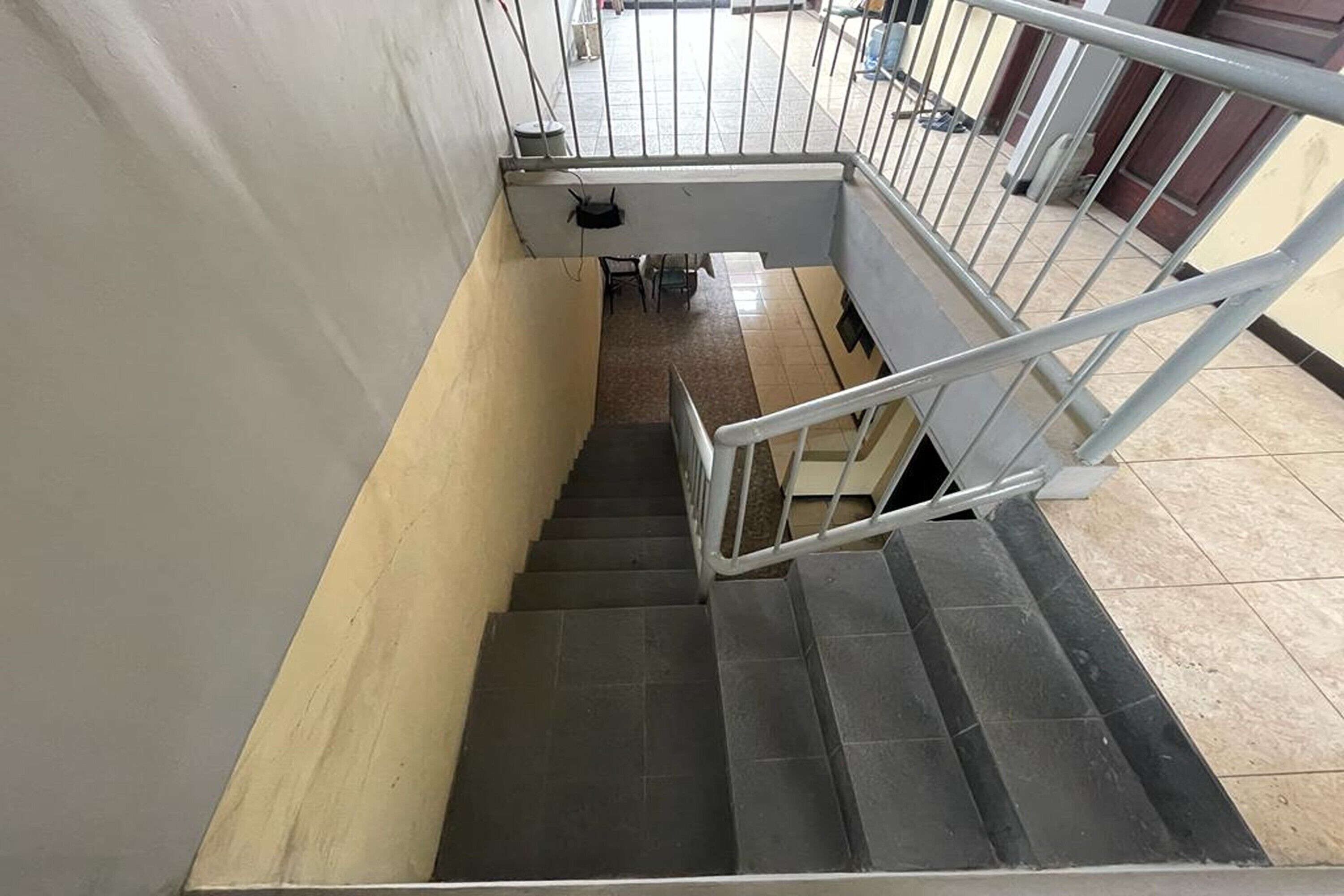 Una escalera con barandilla de metal, pasamanos y una zona de descanso con una silla y una pequeña mesa.