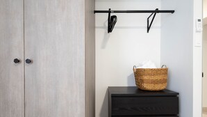 Ein Kleiderschrank mit zwei Türen, eine schwarze Schubladenkommode und ein an der Wand befestigtes Gestell mit einem Korb.