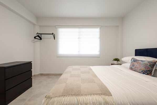 A bedroom with a bed, a dresser, a window with blinds, and a small plant on a nightstand. - Prime Location in San Juan, Puerto Rico – Steps from Everything (San Juan)