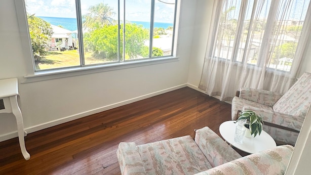 A room with a large window, wooden flooring, and a sofa with a table and plant.