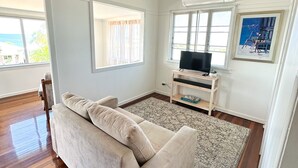 A living room with a beige sofa, a TV on a wooden stand, a patterned rug, and a painting on the wall.