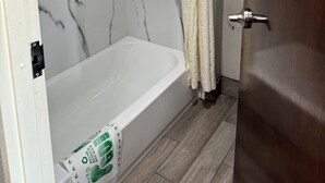 A bathroom with a bathtub, a shower curtain, and a wooden door. - Nola Inn & Suites (New Orleans)