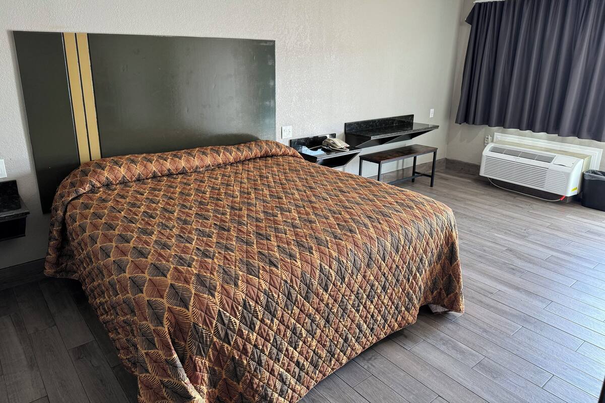 A hotel room with a large bed, a desk, a chair, a flat-screen TV, and a window with curtains.