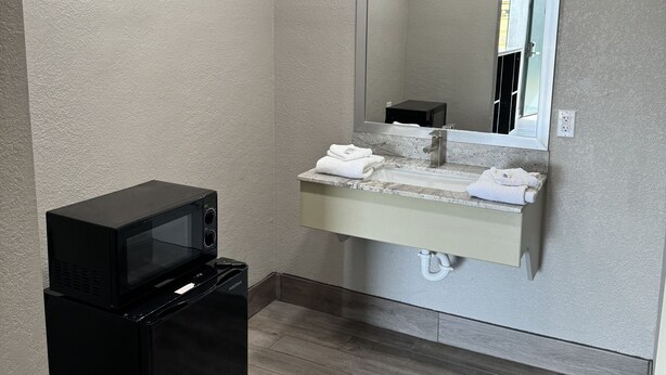 A compact bathroom with a built-in sink, a mirror, and a black microwave on a stand. - Nola Inn & Suites (New Orleans)