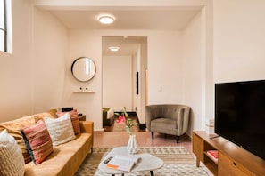 A living room with a sofa, armchair, TV, and a vase with flowers.