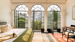 A bedroom with a bed, a desk, and a balcony with large windows. - Santa Casa | Luxury King Room Suite in Roma Norte (Ciudad de México)