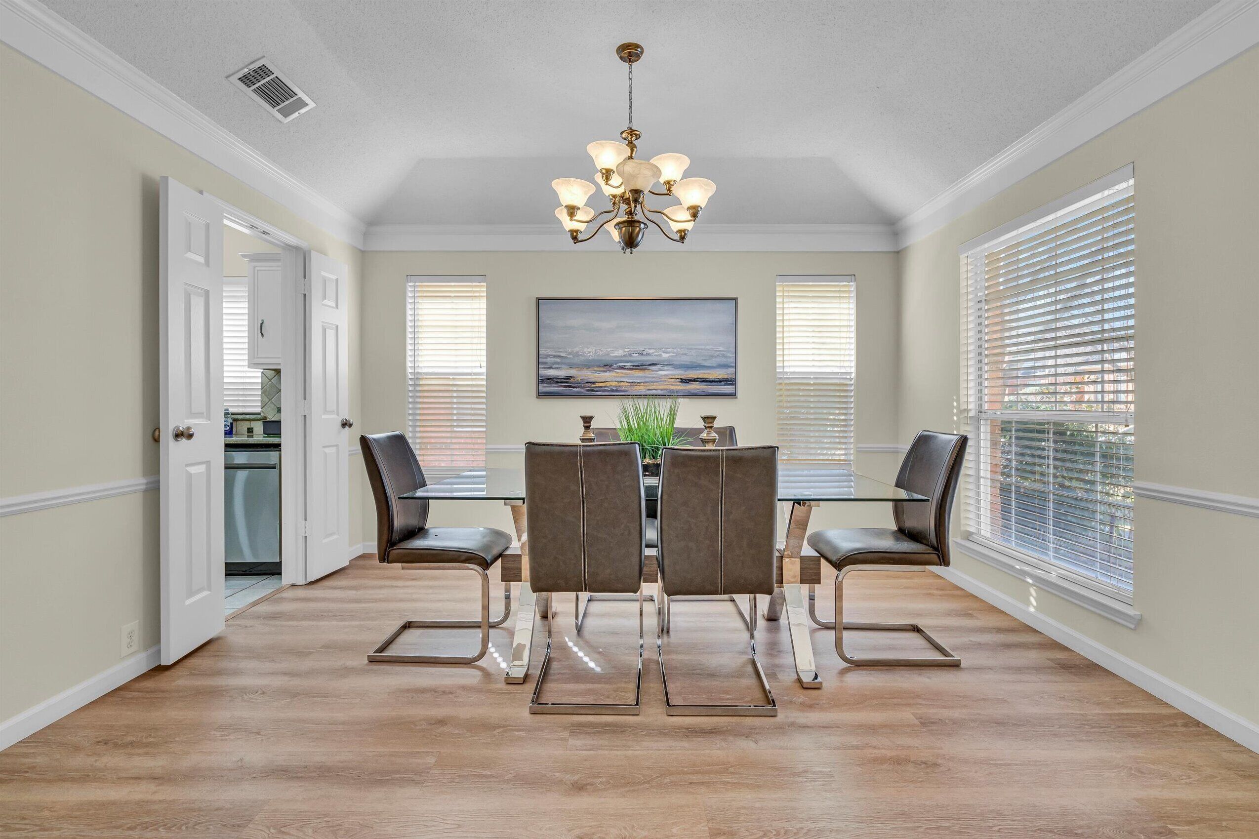 A dining area with a chandelier, a painting, and a view of the outdoors through large windows.