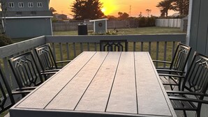 Eine Holzterrasse mit Tisch und Stühlen, die auf einen Garten mit Holzzaun und einem Haus im Hintergrund blickt.