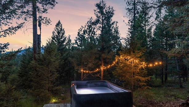 A hot tub on a wooden deck surrounded by trees, with string lights in the background. - A-Frame Glamping. Stargazing Near Missoula (Potomac)