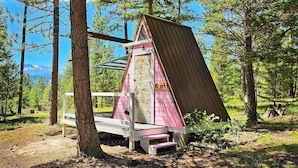 A small, pink, A-frame cabin with a wooden ladder and a bench outside. - A-Frame Glamping. Stargazing Near Missoula (Potomac)