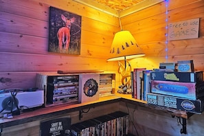 A cozy corner with a wooden wall, a lamp, a collection of books, and a sign indicating free games. - Transforming A-frame Cabin at The Hohnstead Glamping near Missoula, Montana (Potomac)